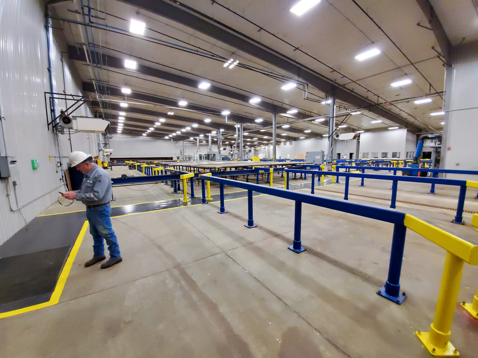 Interior of a large industrial pipe handling and processing bay with overhead lighting and safety railings at a Bakken energy service facility near Williston, North Dakota