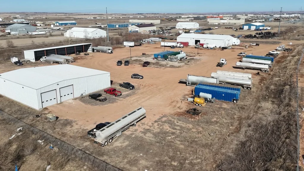 Aerial of 5031 Petroleum Park Dr in Williston, ND: two white industrial shop buildings, covered truck parking and a fenced, stabilized yard